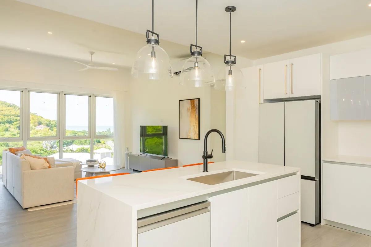 A white open-plan kitchen and living room with glass pendant lights hanging over a long island