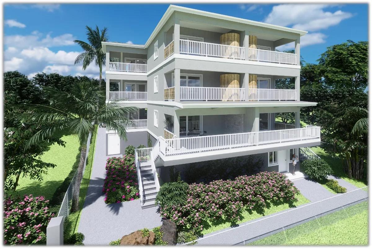 A three-storey white apartment block with stacked balconies, set above flowering shrubs and lawn