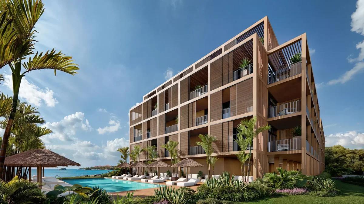 three-quarter view of the building from the garden side, pool and thatched umbrellas at left, sea beyond. 2560x1440