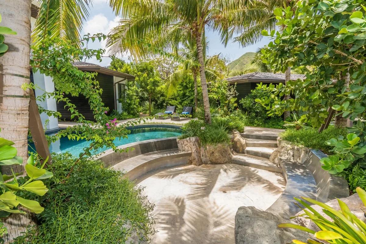 A garden pool edged with boulders and dense tropical planting beside a covered terrace