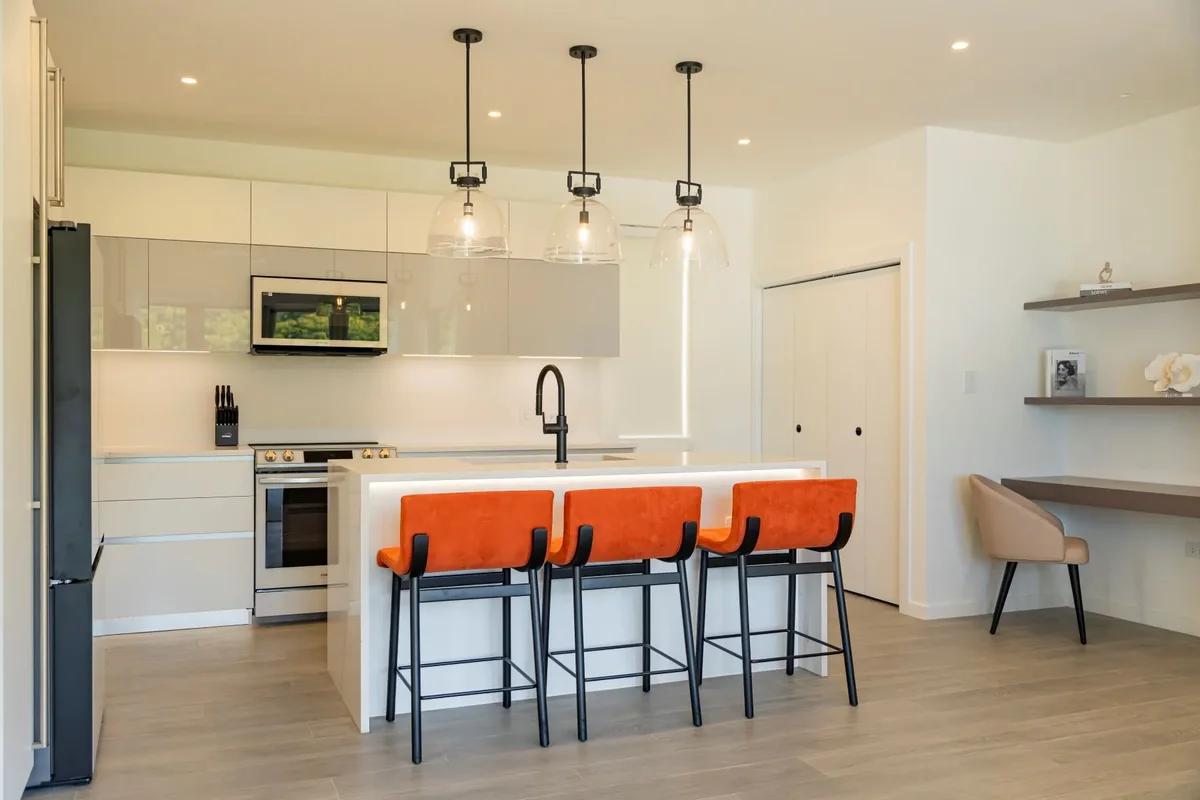A white kitchen with orange bar stools under black pendant lights