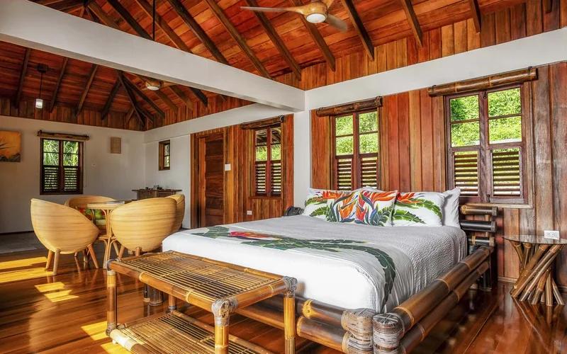 A timber-lined bedroom with louvred windows and a bamboo bench at the foot of the bed