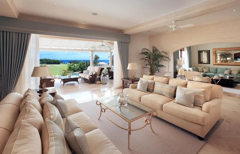 A cream-toned living room with facing sofas opening to a covered terrace and lawn