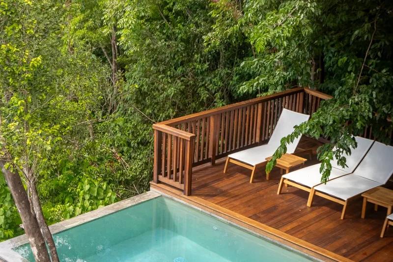 A timber deck with two loungers beside a plunge pool, rainforest closing in behind