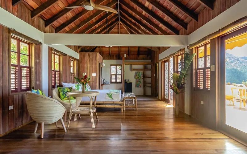 A timber-lined room under a vaulted ceiling with shuttered windows and a small dining set