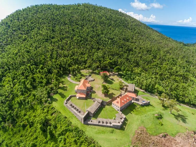 An aerial view of Fort Shirley's restored stone ruins in a forest clearing on Dominica's Cabrits headland, with the sea beyond