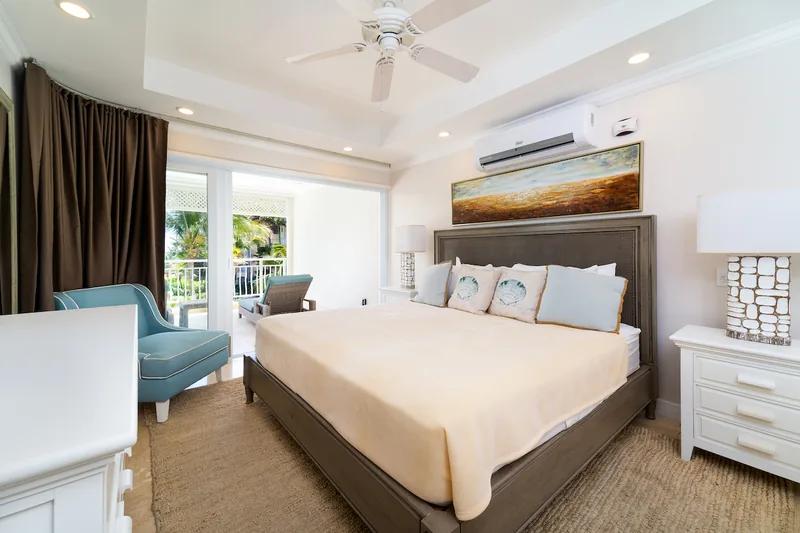 A bedroom with a dark upholstered headboard, a blue chaise and doors to a balcony