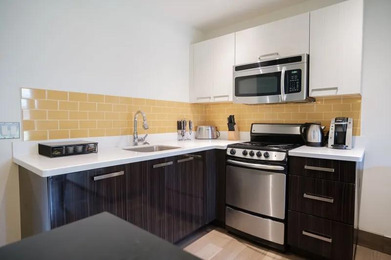 A compact kitchen with dark cabinets, a stainless range and a tiled splashback
