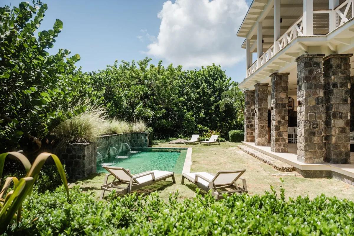 A stone-columned villa above a garden pool at Christophe Harbour, two loungers set out on the lawn