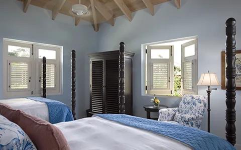 A blue bedroom with a mahogany four-poster bed and white shuttered windows