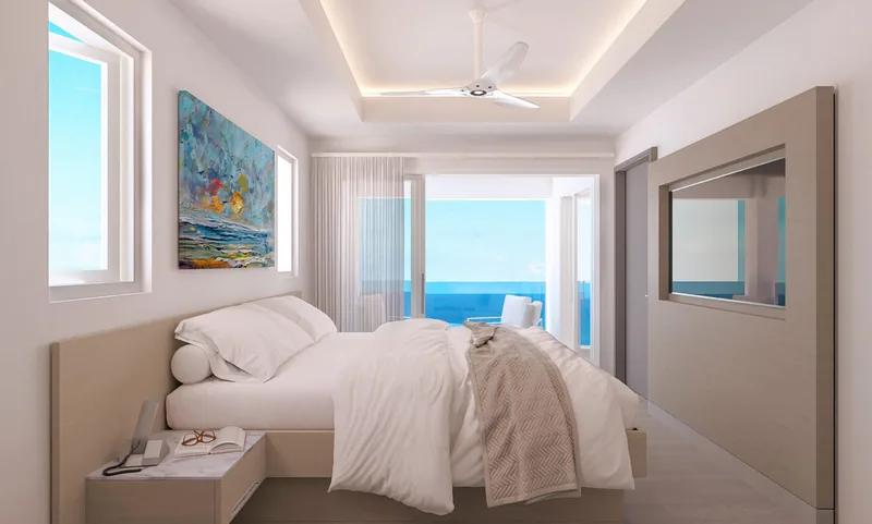 A white bedroom with a framed painting and a window looking out to the sea