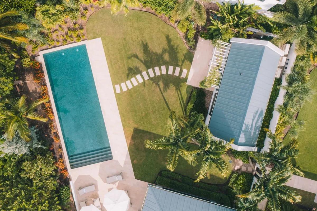 Two pools and a lawn seen from directly above, palm shadows falling across the grass