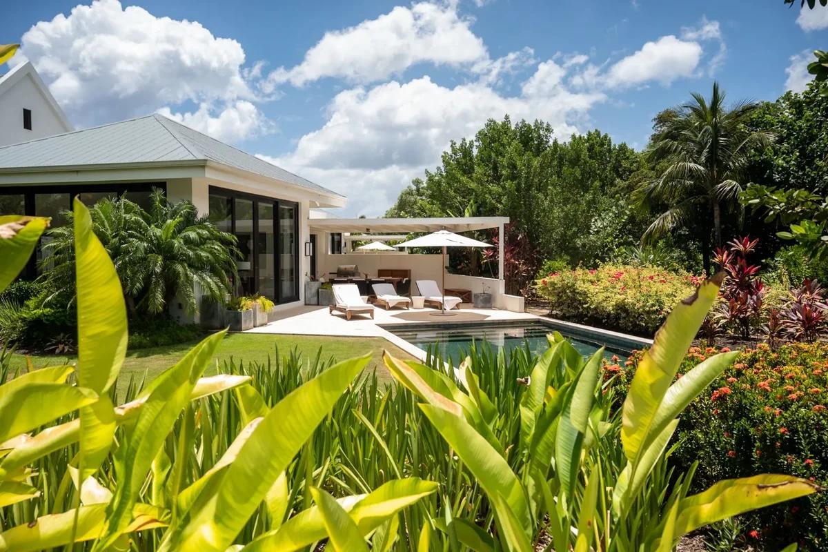 A white beachfront villa at Pinney's Beach, Nevis, its pool and shaded terrace seen through heliconia and palms