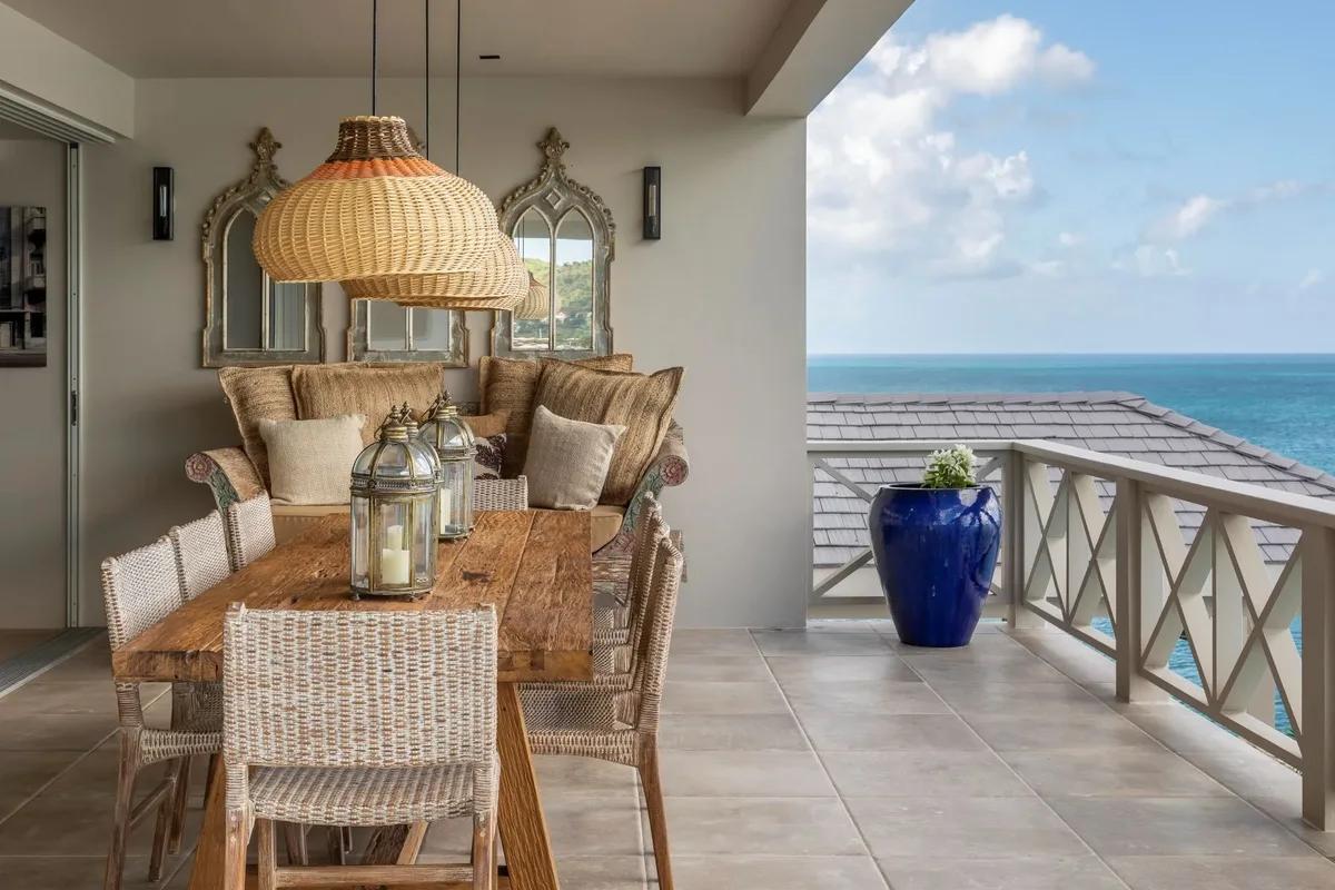 A dining table under a rattan pendant beside a balustrade and the sea