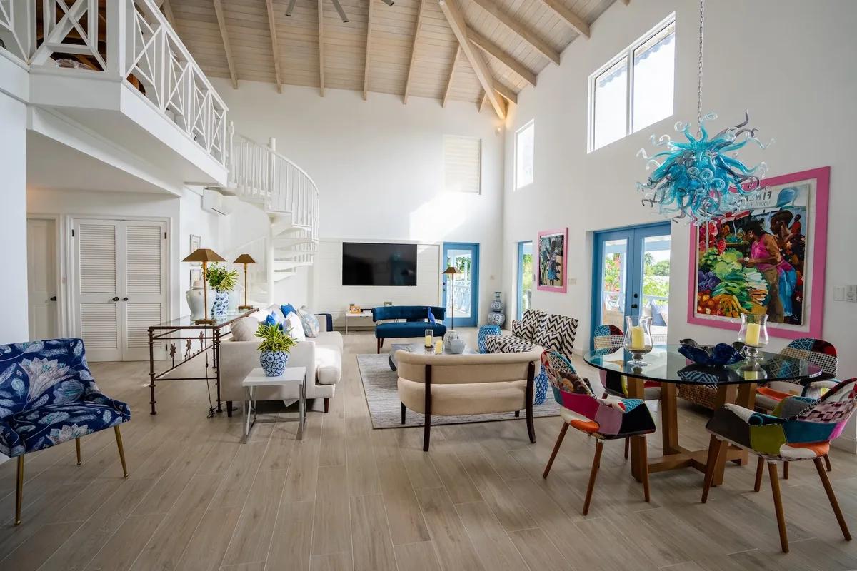A double-height living room with bright contemporary art and a mix of coloured dining chairs