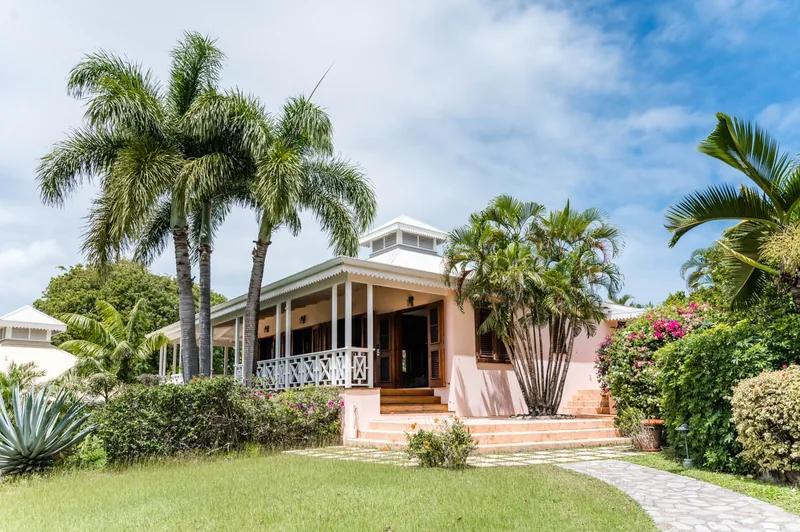 A pink house with a white verandah among palms and flowering shrubs