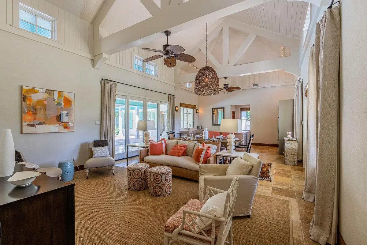 A living room under a vaulted white ceiling with a ceiling fan and patterned rattan seating