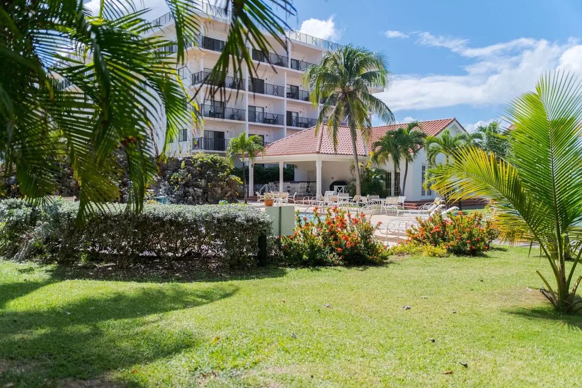 A lawn with flowering shrubs and palms in front of a low apartment block