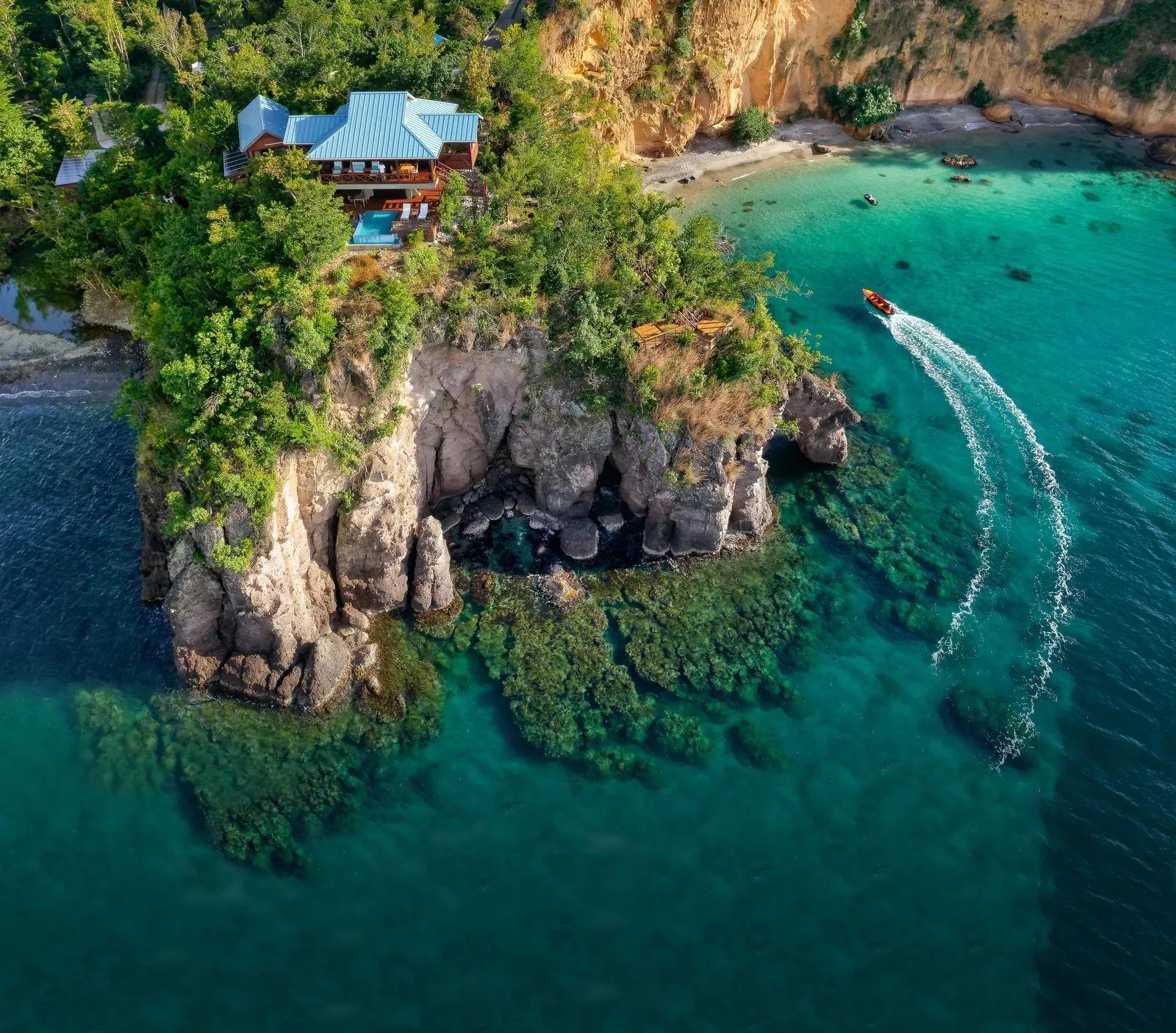 A timber villa on a rocky Dominican headland above a cove, a boat cutting across the bay