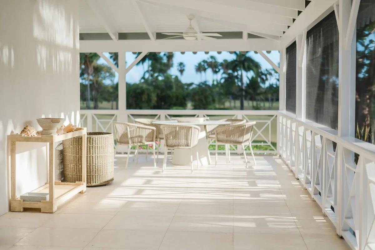 A white covered verandah with wicker seating and lanterns, looking out across a lawn to palms