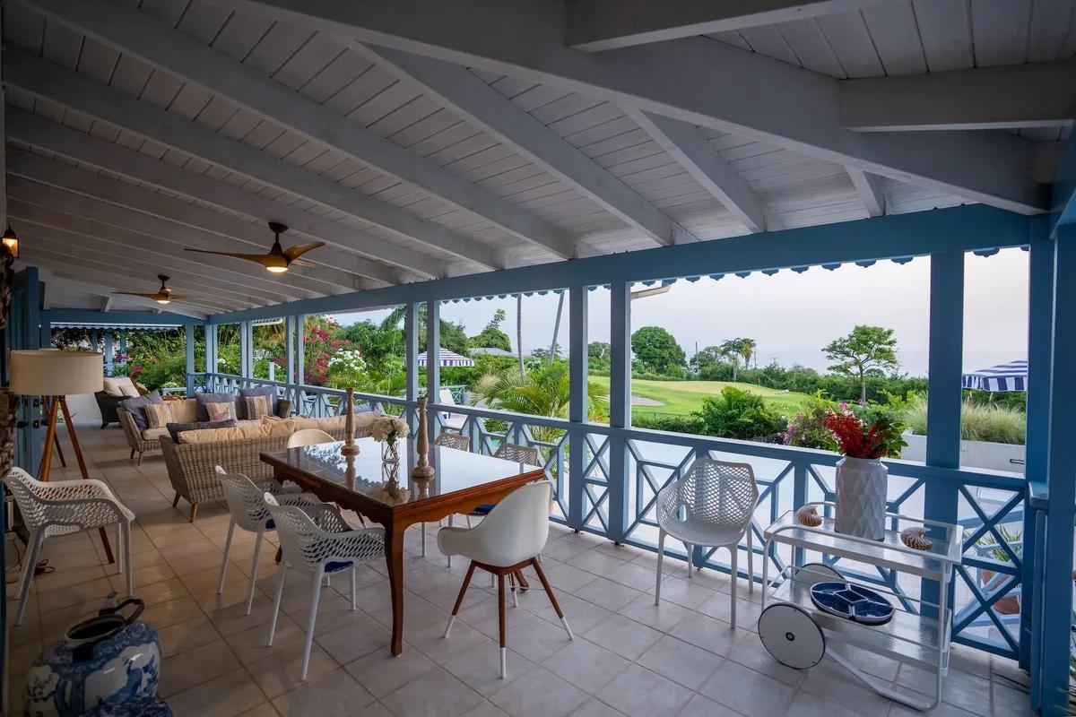 A blue and white colonnaded verandah with a dining table, ceiling fans and open country beyond