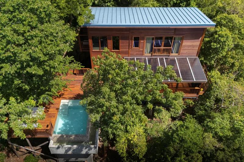 A timber villa with a blue metal roof set in rainforest canopy, its plunge pool on the deck below