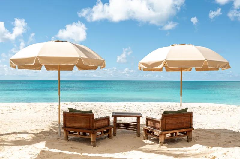 Two cream parasols and timber day-beds on a white beach above clear shallows