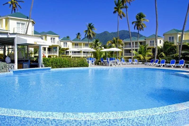 A circular pool with blue loungers in front of pastel apartment buildings and palms