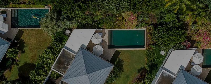 Villa roofs and two plunge pools seen from directly above among dense garden