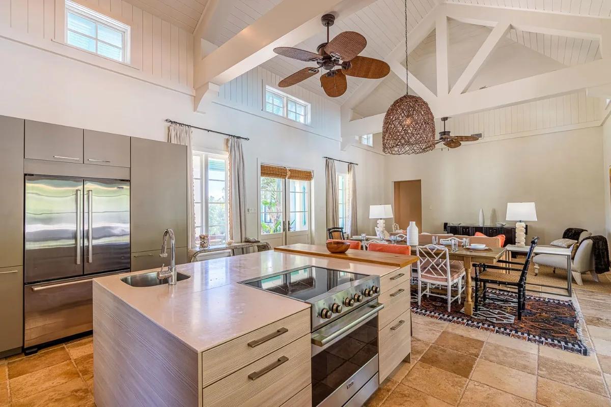 A kitchen with a long island under a vaulted white ceiling and a palm-leaf ceiling fan