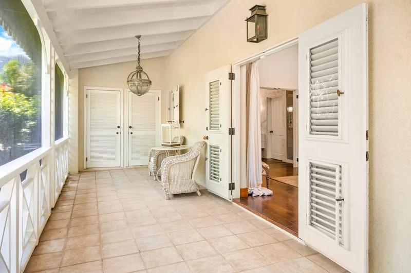 A tiled hallway with louvred doors, a pendant lantern and windows down one side
