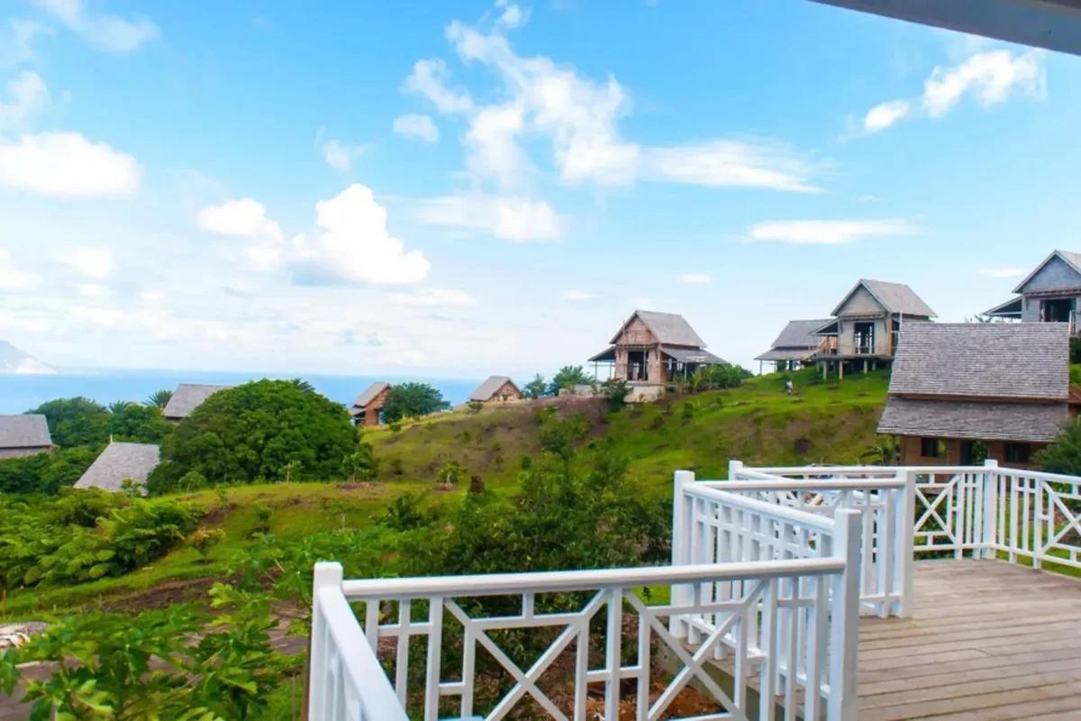 A white balcony rail looking across green hillside to timber cottages with steep pitched roofs
