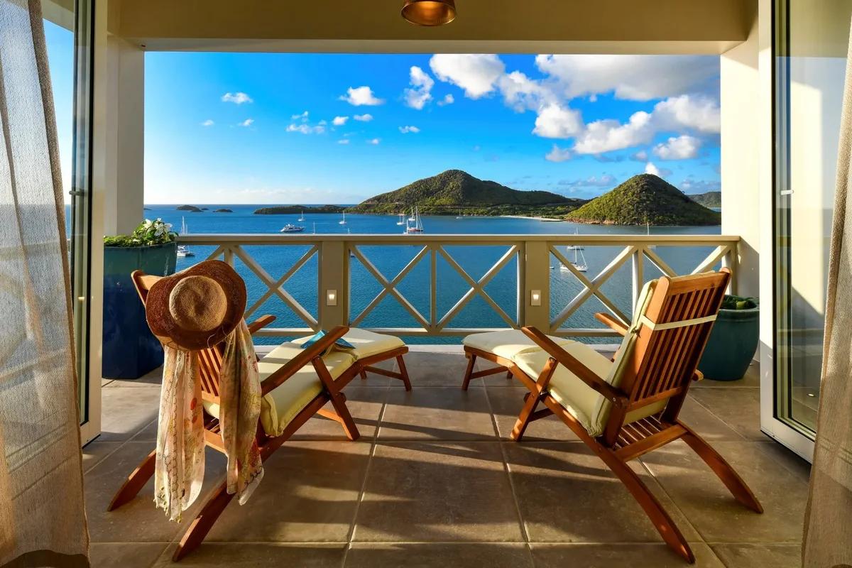 Two timber chairs and a straw hat on a balcony looking across to a green island