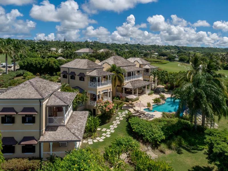 Stone-faced villas with balconies set around a pool and palms, seen from the air