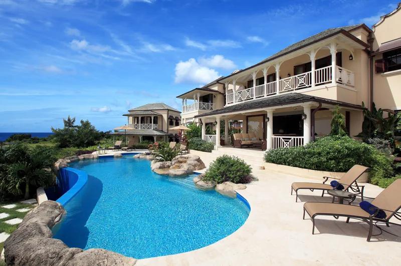 A coral-stone villa with balconied wings above a curving free-form pool and loungers