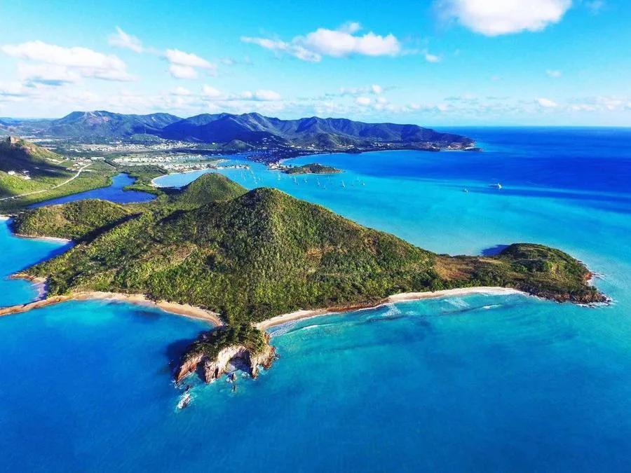 A green Antiguan headland with a curving beach and turquoise reef, seen from the air