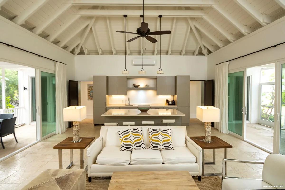 A living room under a white vaulted timber ceiling, sofas and table lamps between open glass doors