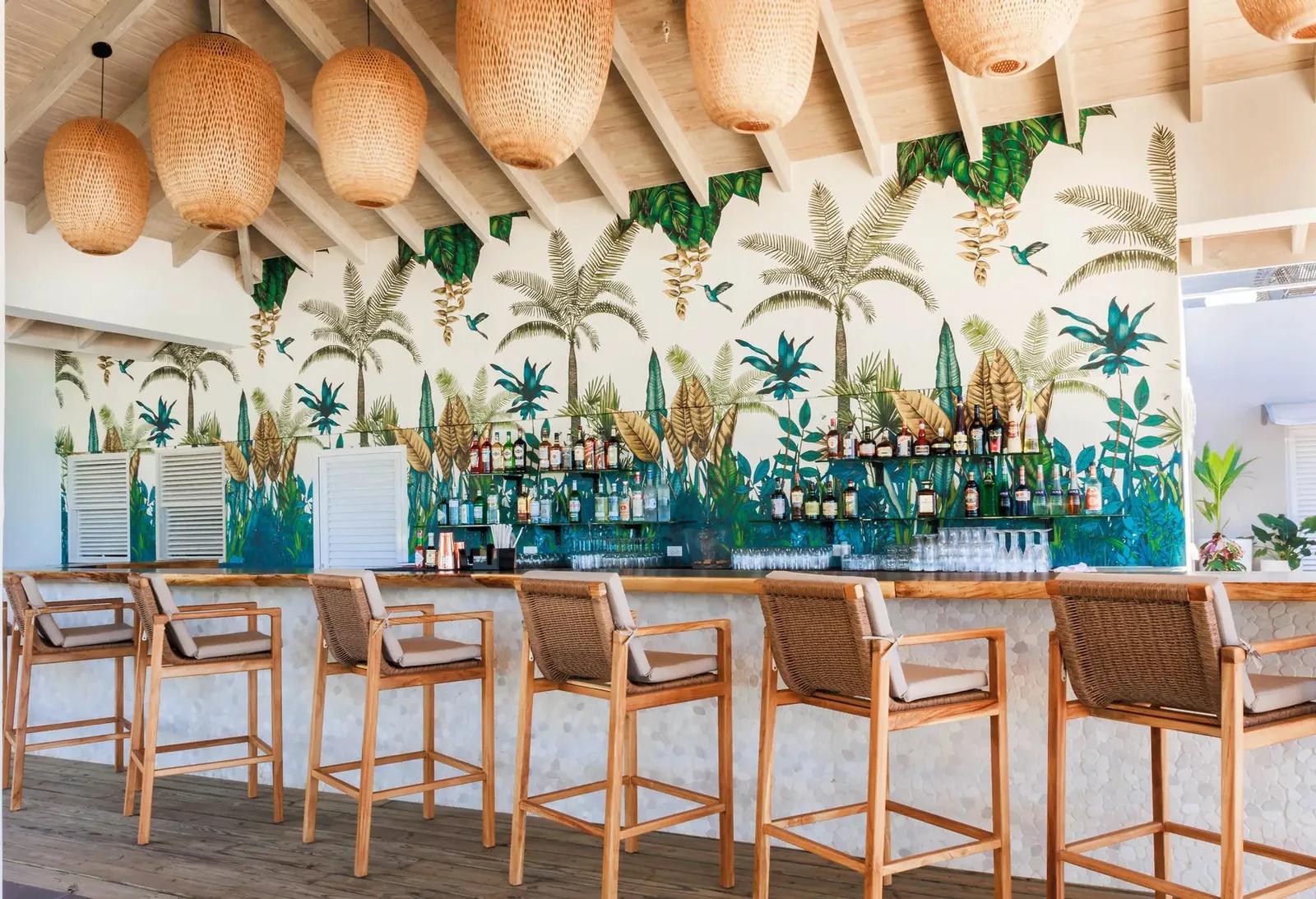 A bar counter with woven pendant lights and a painted palm mural behind the bottles