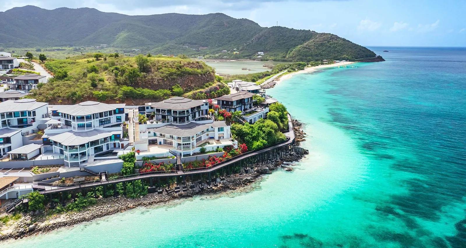 White condominiums along a green headland above a turquoise bay, a beach curving away