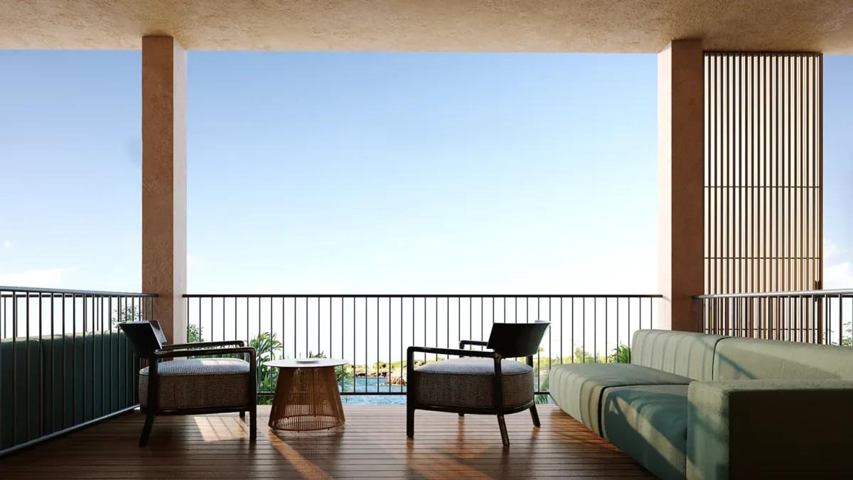 A covered balcony with two armchairs and a low table beside a green sofa, the sea beyond the railing