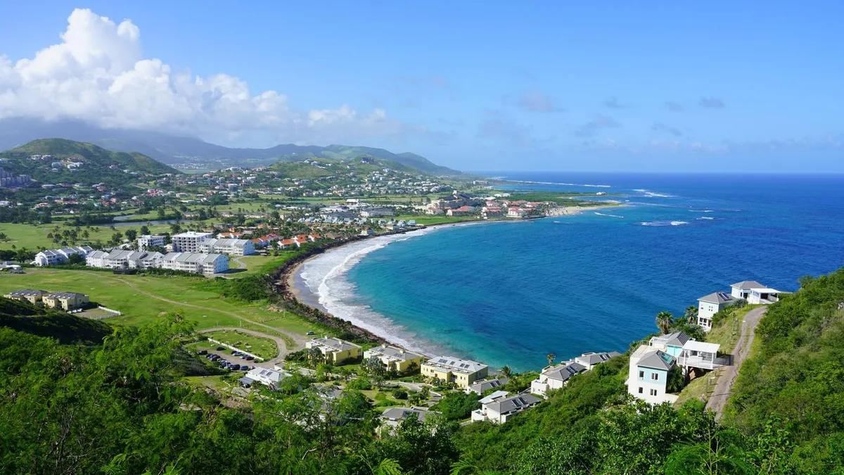 The long curve of a St Kitts bay seen from the hills, villas among the greenery above the shore