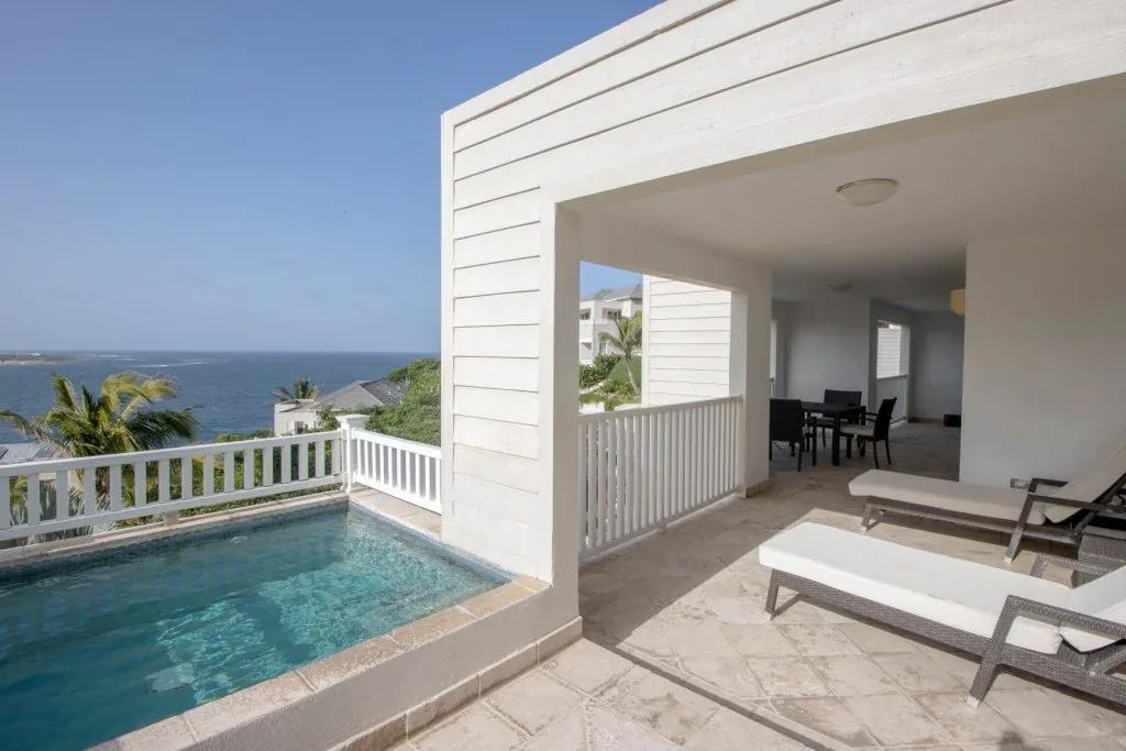 A terrace pool with loungers behind a white balustrade, the sea and a headland beyond