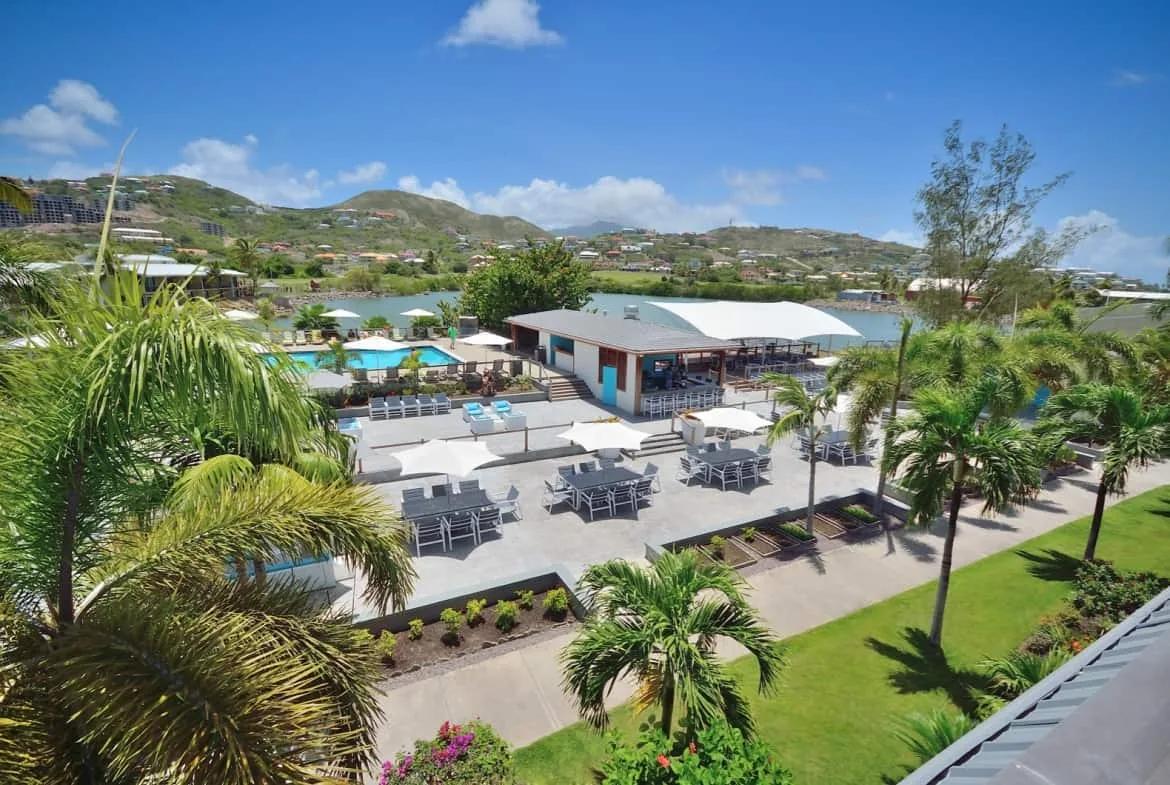 The pool deck and open-air poolside bar at the Royal St Kitts, with loungers, dining terraces and the hills of Frigate Bay beyond a salt pond
