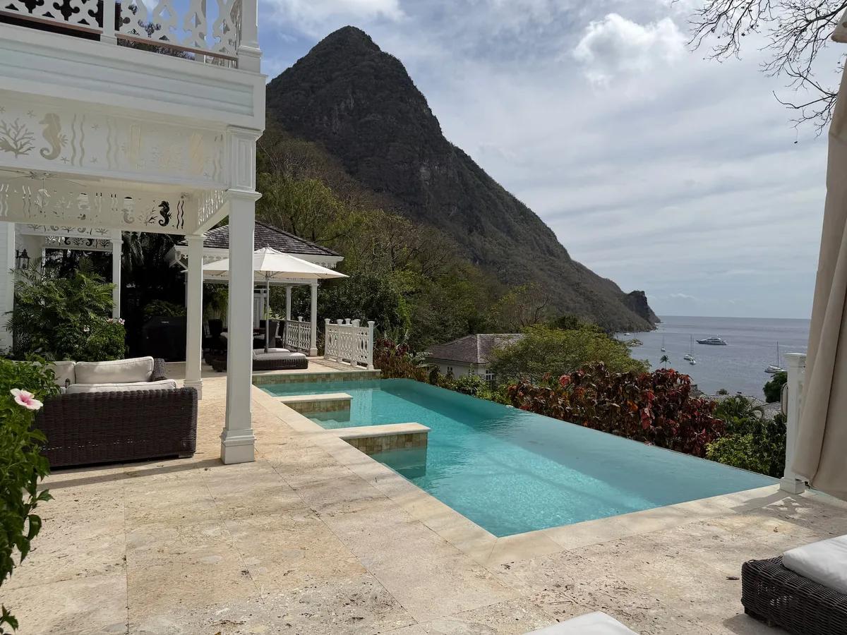 A white colonial verandah beside a pool, a Piton rising directly behind